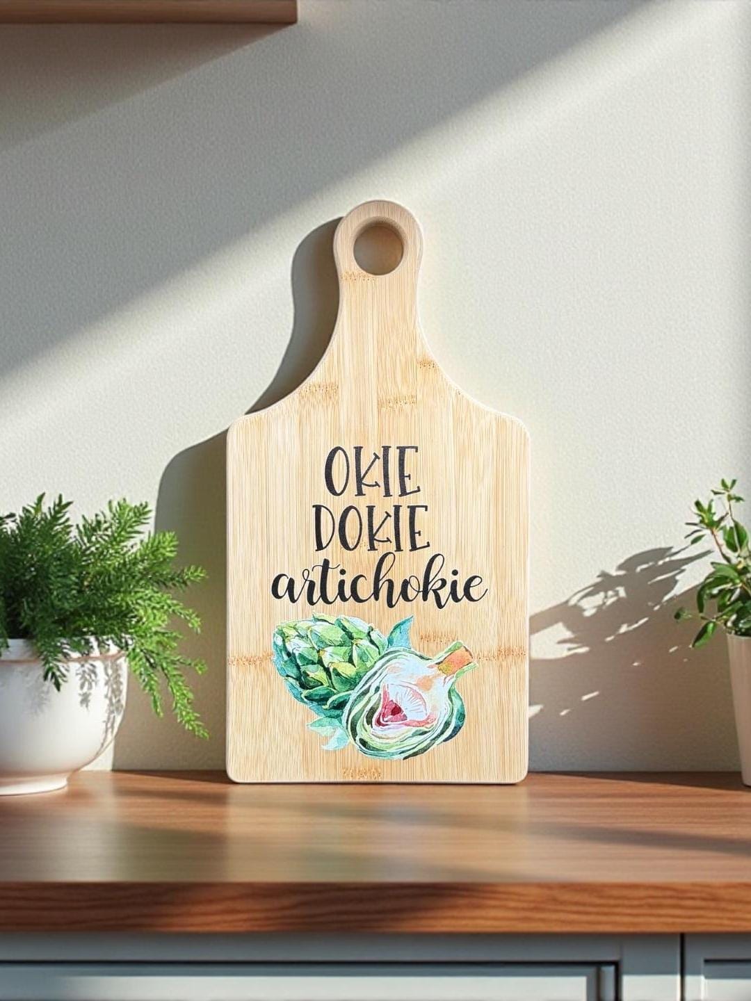 Decorative bamboo paddle board with artichoke illustration and the words “Okie Dokie Artichokie”.