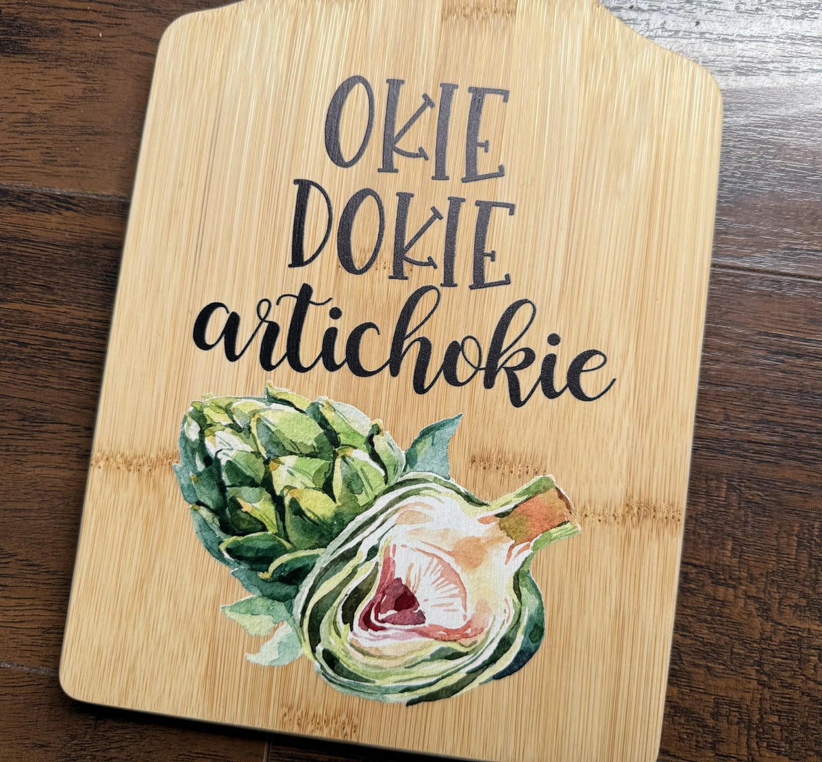 Decorative bamboo paddle board with artichoke illustration and the words “Okie Dokie Artichokie”.