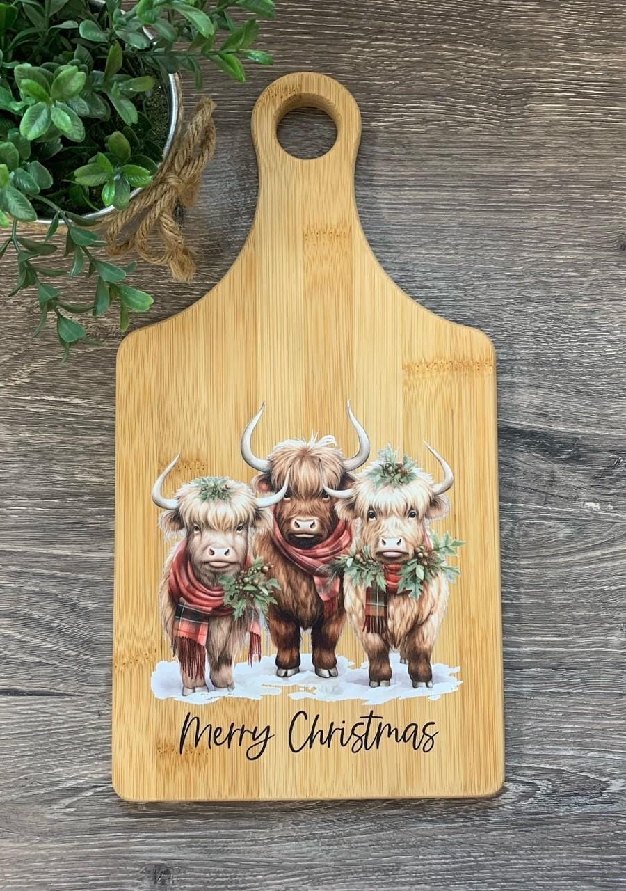 Decorative bamboo paddle board with three festive Highland cows.