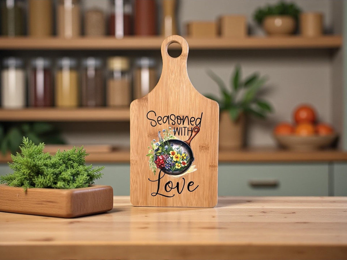 Decorative bamboo paddle board with floral artwork and the words “Seasoned With Love”.