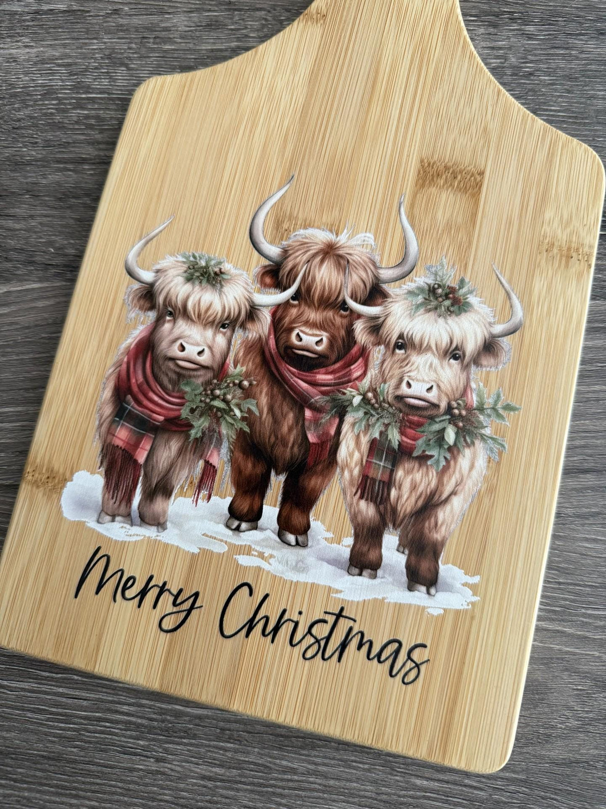 Decorative bamboo paddle board with three festive Highland cows.