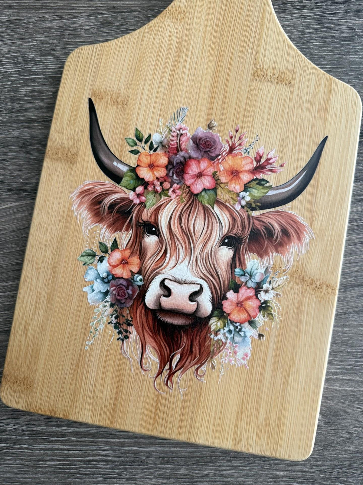 Decorative bamboo paddle board with Highland cow surrounded by flowers.