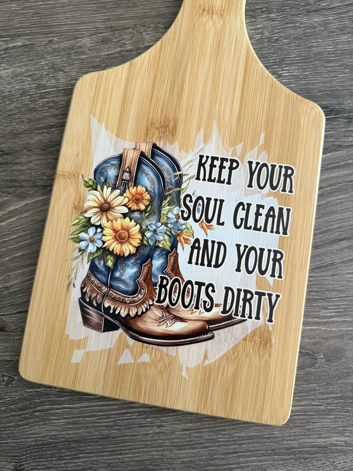 Decorative bamboo paddle board with floral cowboy boots and the words “Keep Your Soul Clean and Your Boots Dirty”.