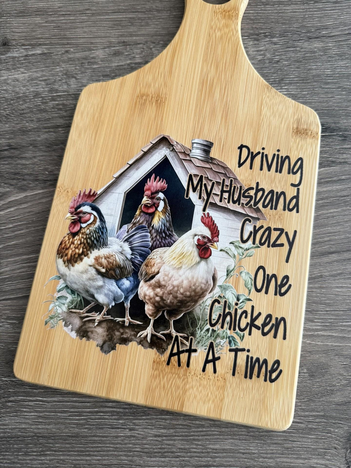 Decorative bamboo paddle board with chicken illustration and the words “Driving My Husband Crazy One Chicken at a Time”.