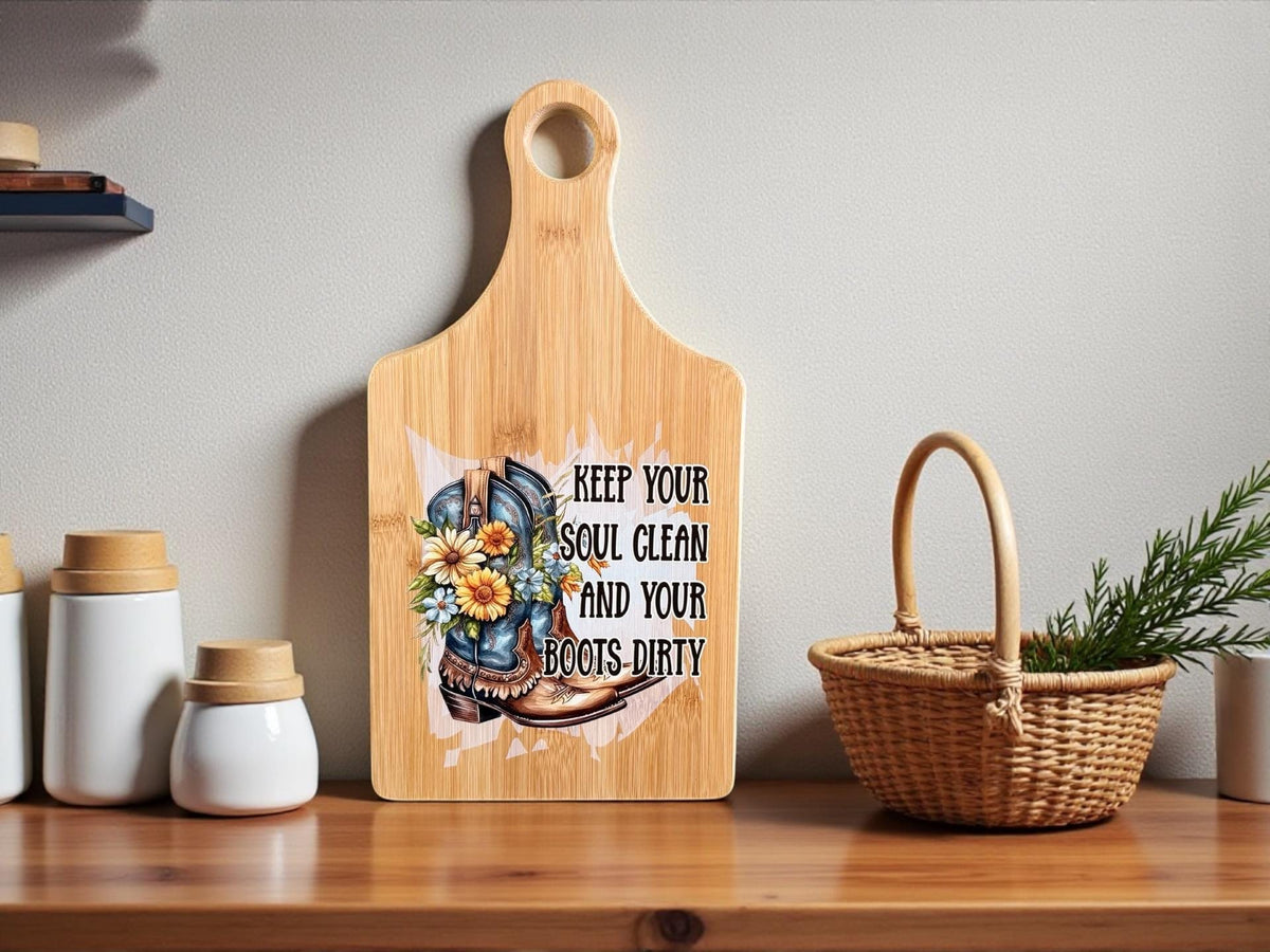 Decorative bamboo paddle board with floral cowboy boots and the words “Keep Your Soul Clean and Your Boots Dirty”.