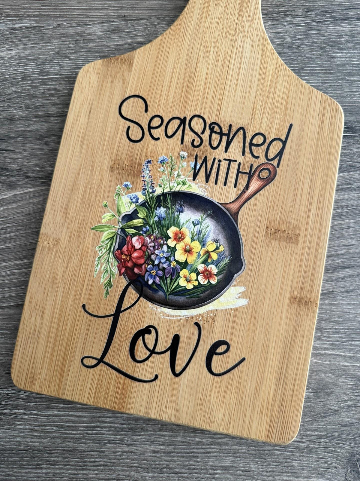 Decorative bamboo paddle board with floral artwork and the words “Seasoned With Love”.