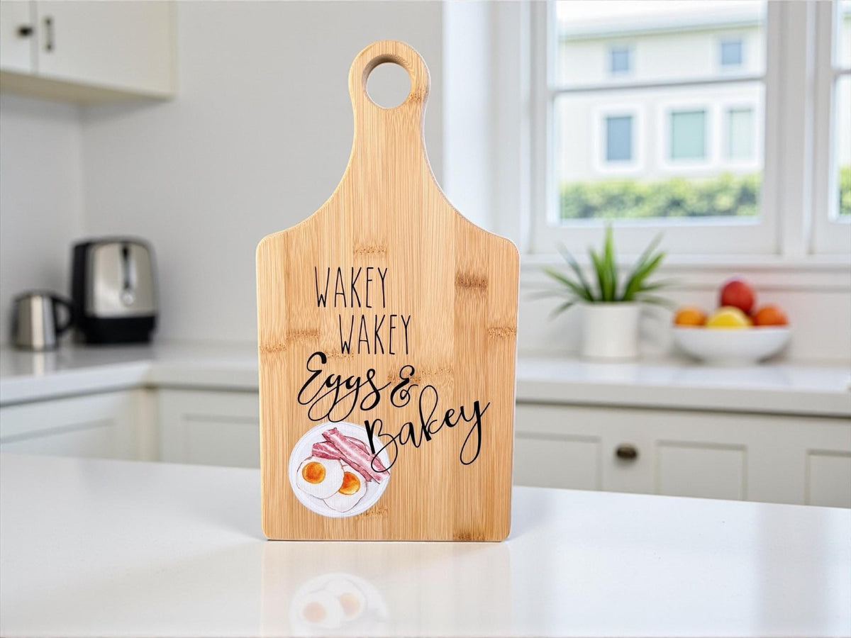 Decorative bamboo paddle board with breakfast-themed lettering and the words “Wakey Wakey Eggs and Bakey”.