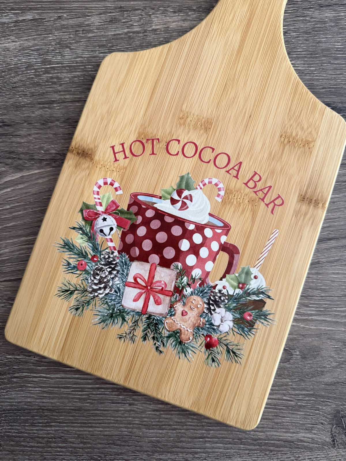 Decorative bamboo paddle board with hot cocoa mug with candy canes and the words “Hot Cocoa Bar”.