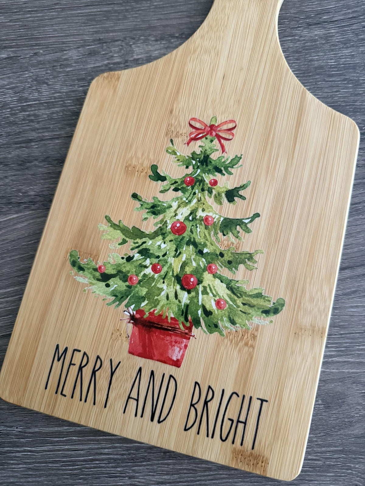 Decorative bamboo paddle board with festive Christmas design and the words “Merry and Bright”.