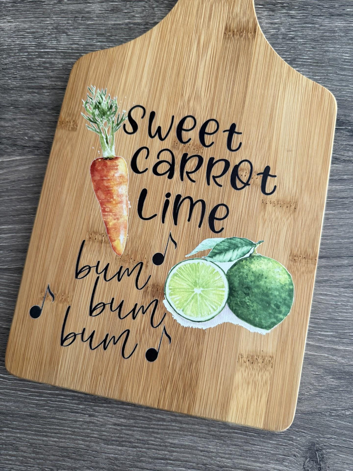 Decorative bamboo paddle board with carrot and lime artwork and the words “Sweet Carrot Lime”.