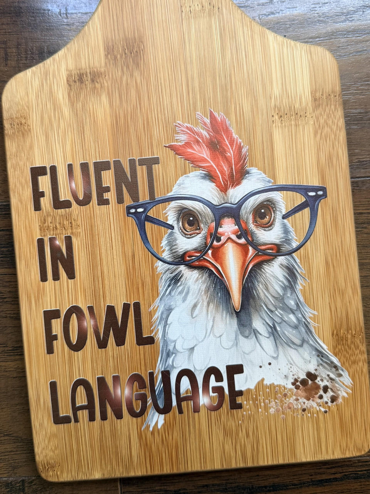 Decorative bamboo paddle board with chicken illustration and the words “Fluent in Fowl Language”.