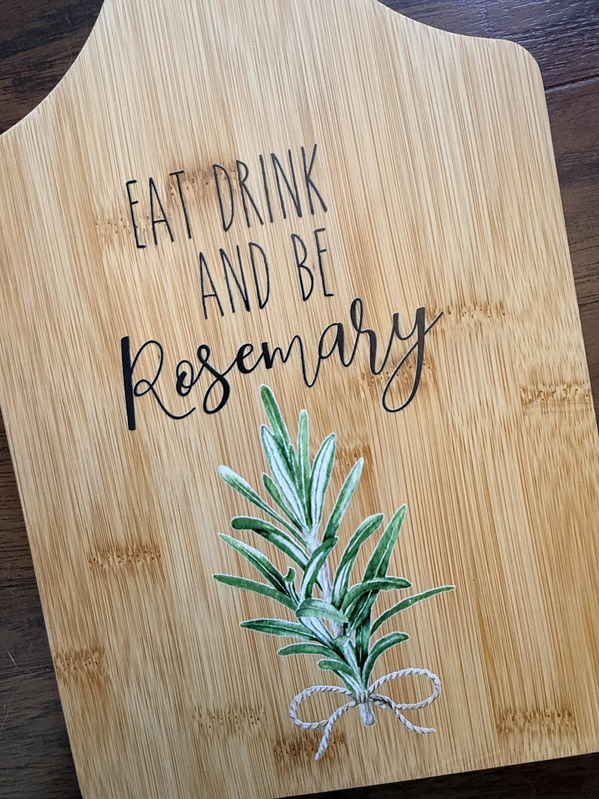 Decorative bamboo paddle board with rosemary sprig and the words “Eat, Drink and Be Rosemary”.