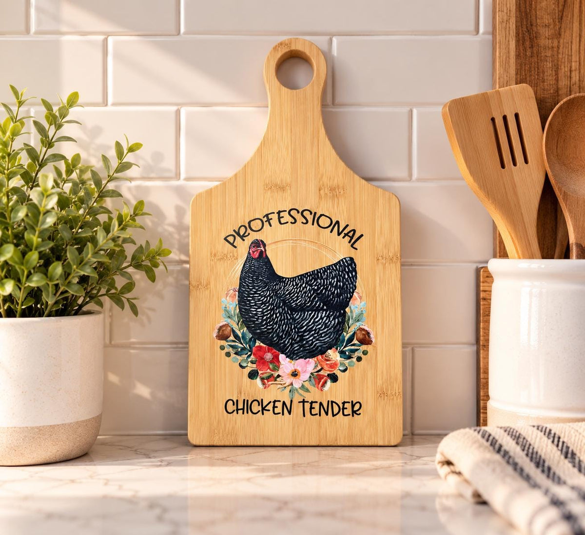 Decorative bamboo paddle board with chicken and floral artwork and the words “Professional Chicken Tender”.