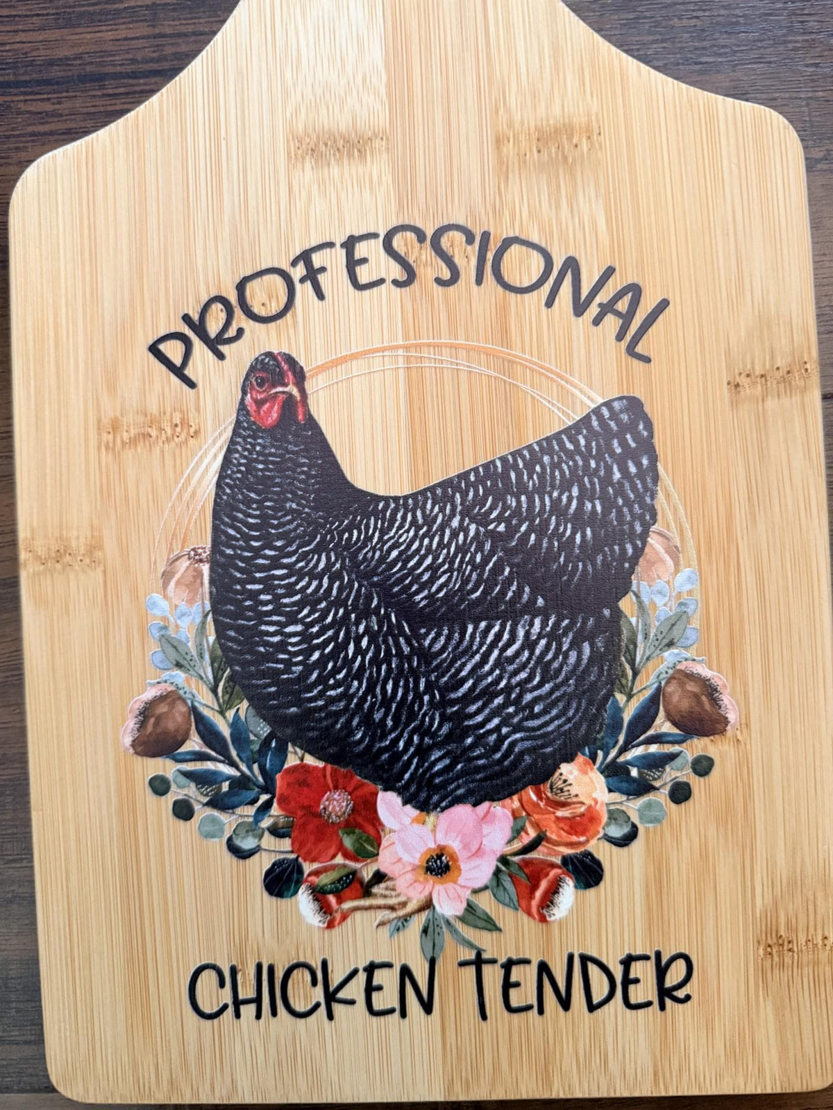 Decorative bamboo paddle board with chicken and floral artwork and the words “Professional Chicken Tender”.