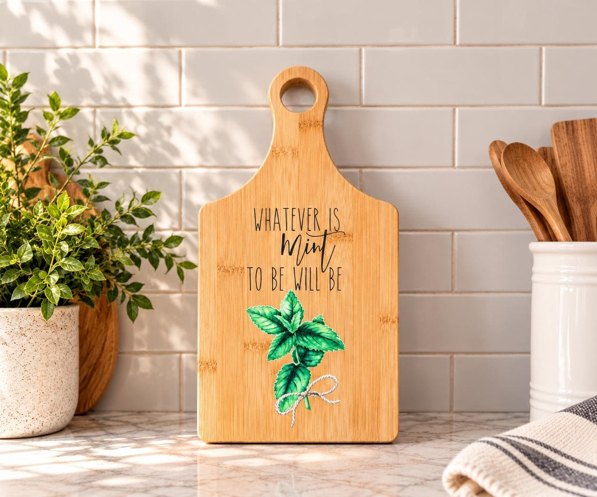 Decorative bamboo paddle board with mint herb sprig and the words “Whatever Is Mint to Be Will Be”.