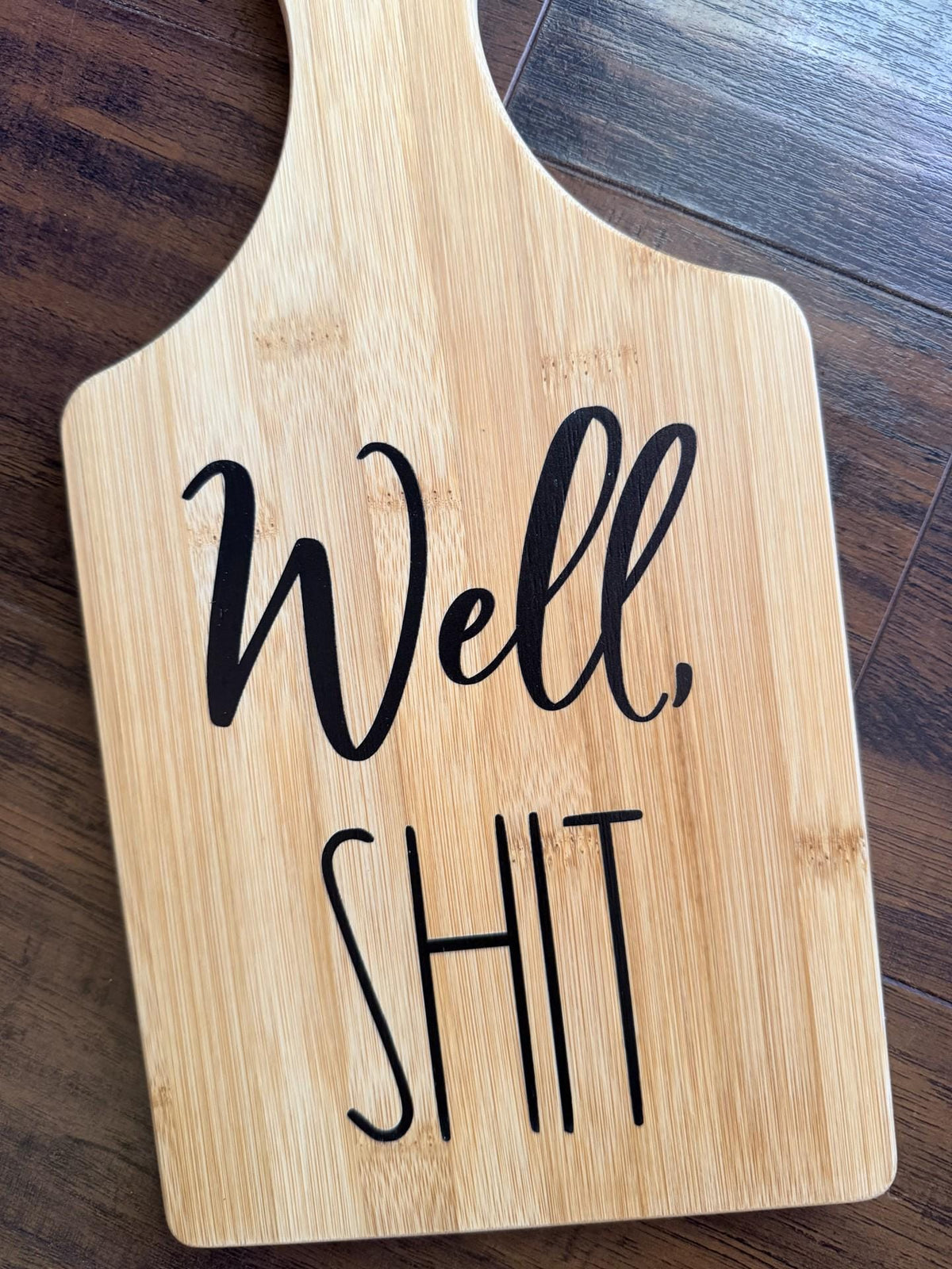 Decorative bamboo paddle board with bold humorous lettering and the words “Well, Shit”.