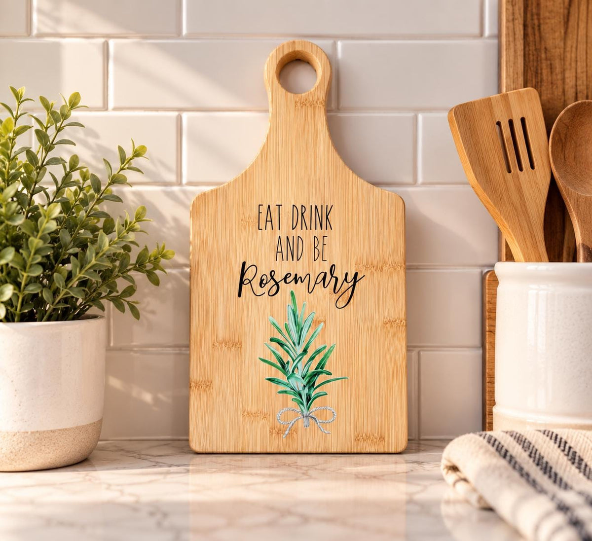Decorative bamboo paddle board with rosemary sprig and the words “Eat, Drink and Be Rosemary”.
