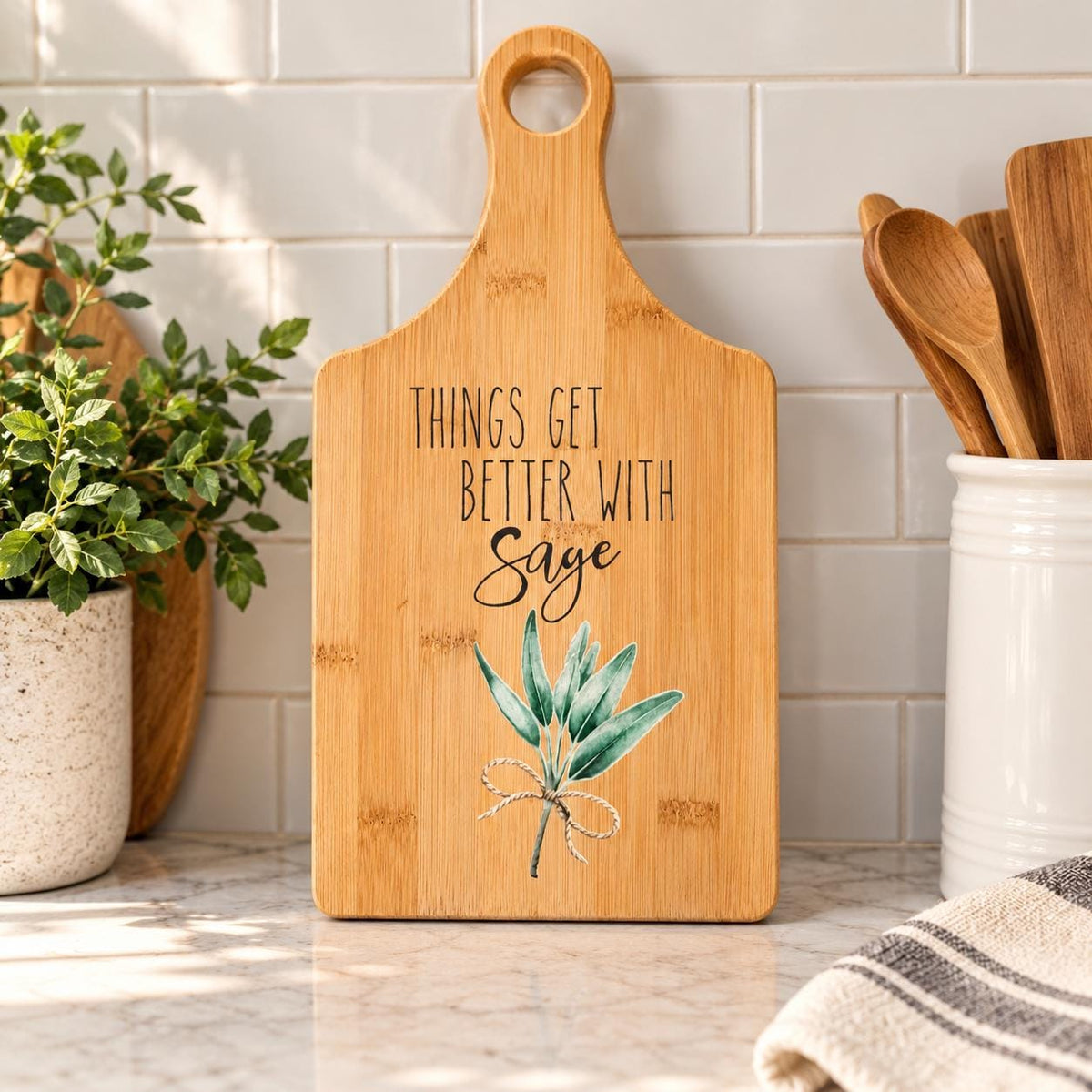 Decorative bamboo paddle board with sage herb sprig and the words “Things Get Better With Sage”.