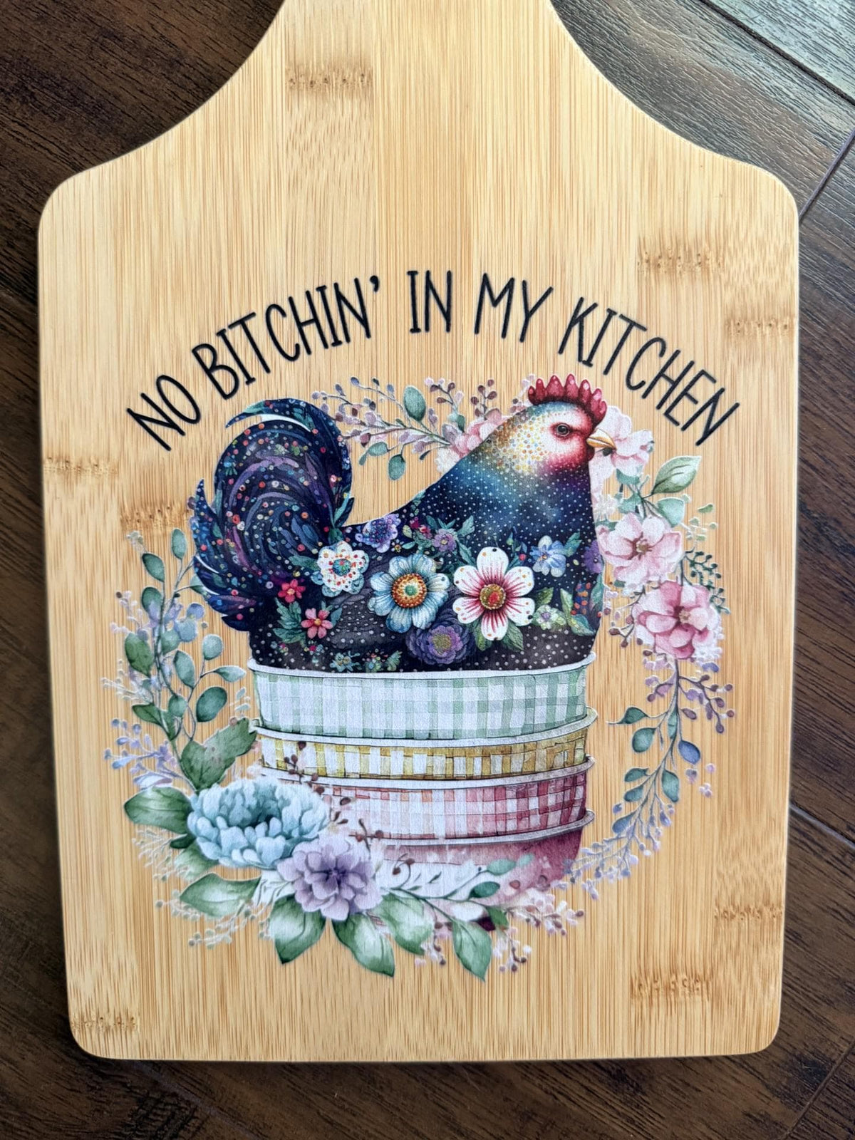 Decorative bamboo paddle board with chicken illustration and the words “No Bitchin' in My Kitchen”.