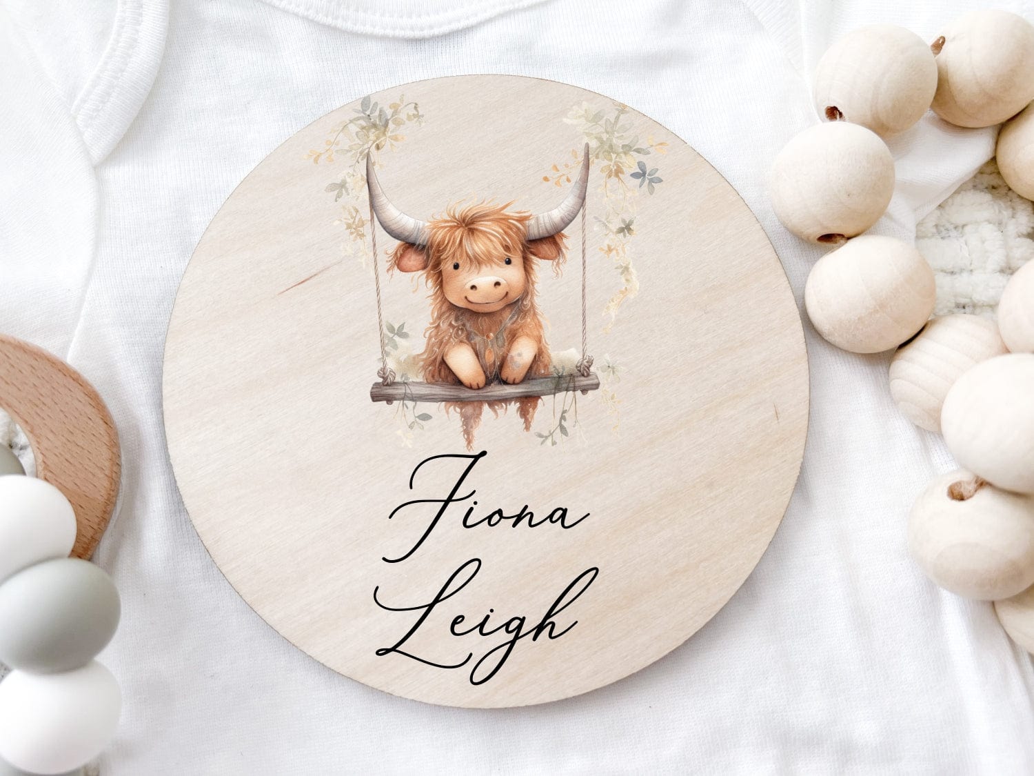 round wood baby name sign printed with a baby highland cow on a swing with the child's name below