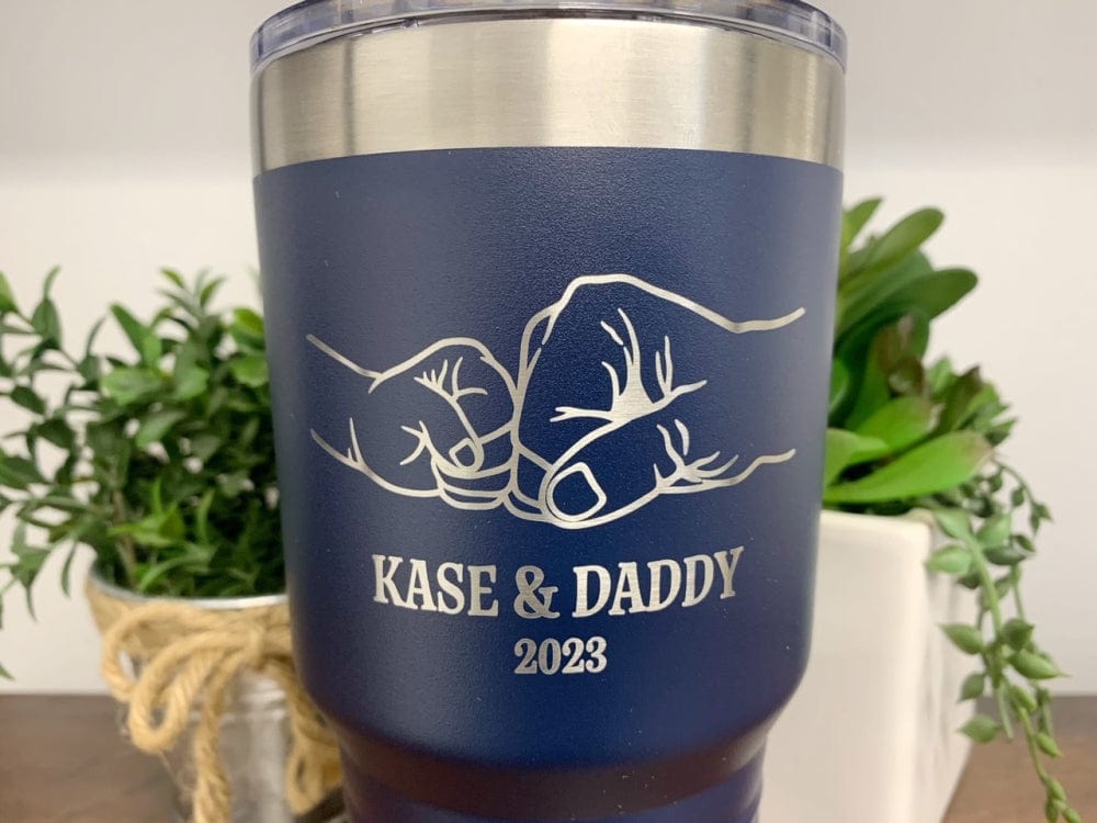 Close up of 30oz navy blue tumbler featuring an engraved fist bump design, personalized with names of a child and dad, along with the year.