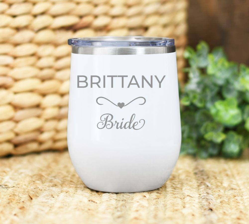 12oz wine tumbler laser engraved with name in all caps with heart design under and then wedding party title (bride etc.). shown on white